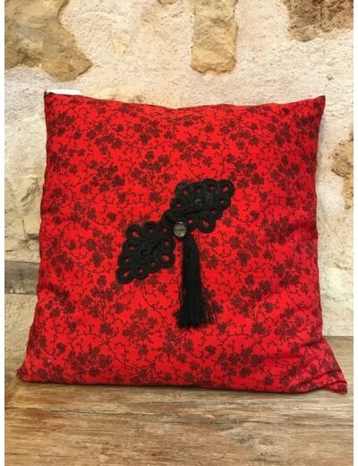 Housse de coussin rouge avec des fleurs noires, un ornement, un pompon et un bouton.